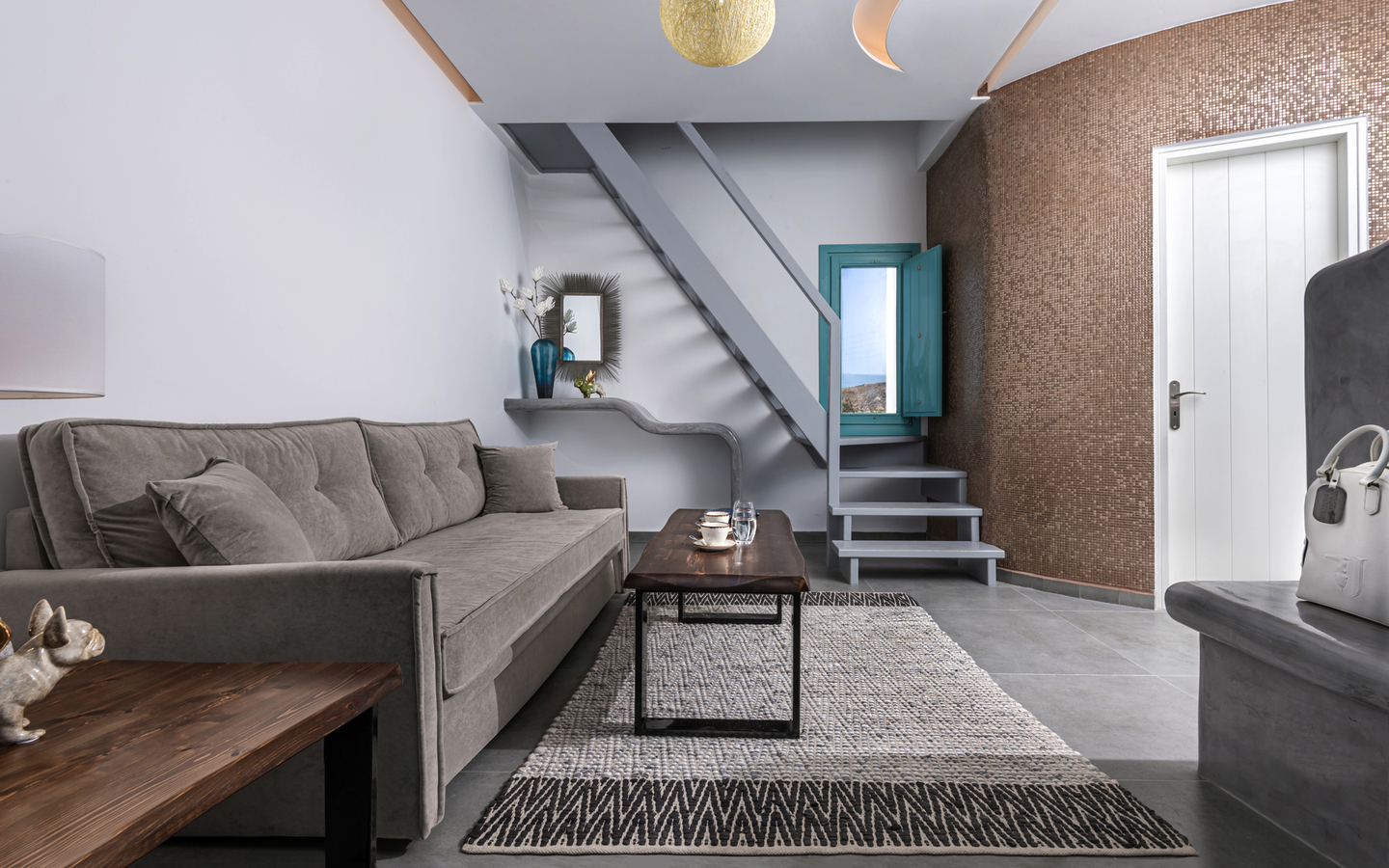 Modern eingerichtetes Zimmer mit Sofa, Treppe, Teppich und einer weißen Tür.