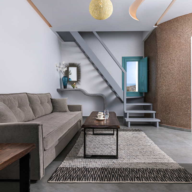 Modern eingerichtetes Zimmer mit Sofa, Treppe, Teppich und einer weißen Tür.