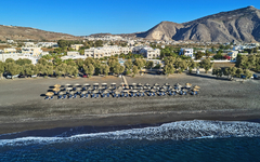 Strand mit Liegestühlen und Sonnenschirmen vor Hotel und Bergen im Hintergrund.