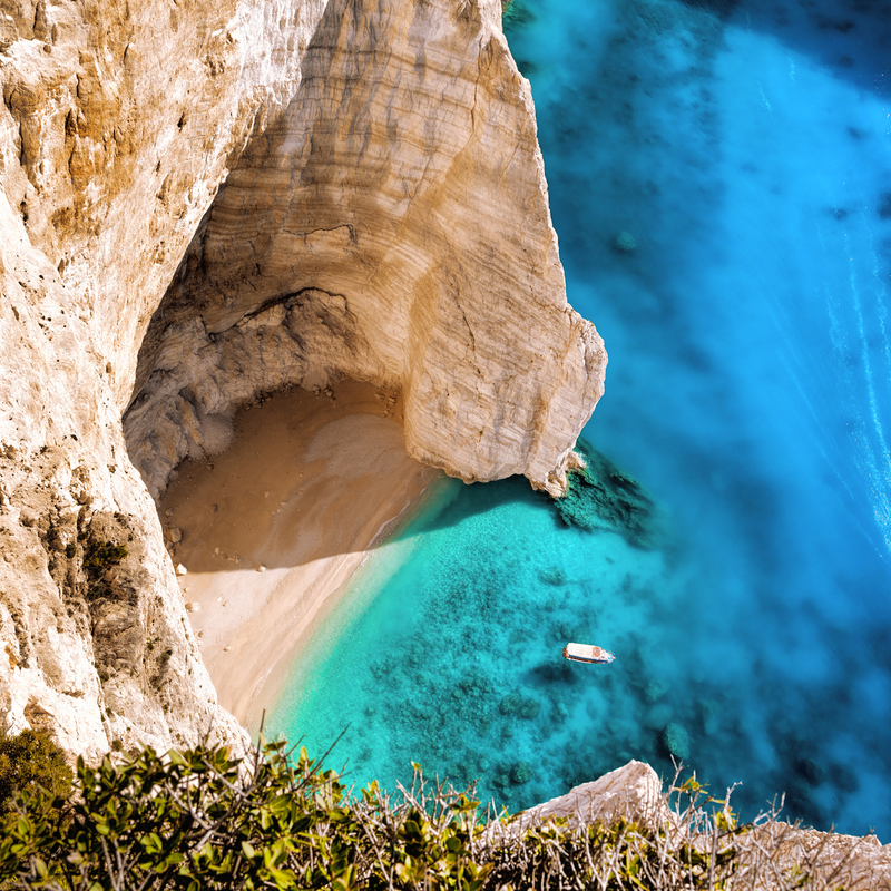 Steilküste mit klarem blauen Wasser und kleinem Boot.