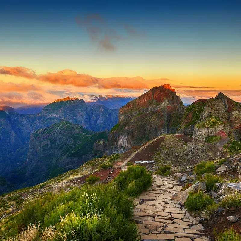 Blick auf den Berg Pico Ruivo auf Madeira während des Sonnenuntergangs, umgeben von Bergen, mit einem Wanderweg im Vordergrund.
