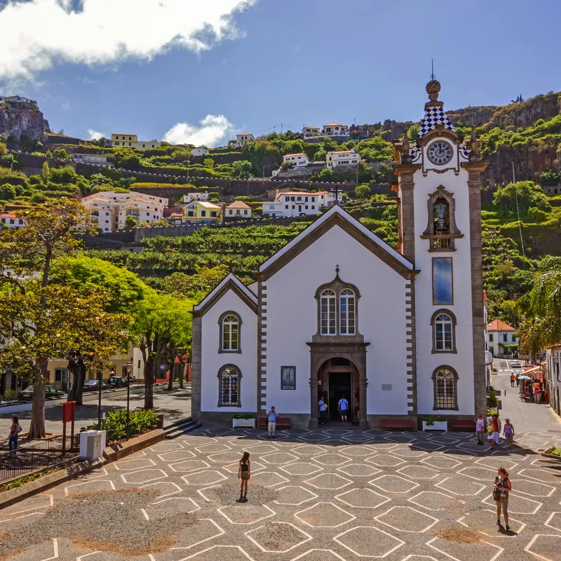 Kirche mit Turm vor grüner Berglandschaft und blauen Himmel.