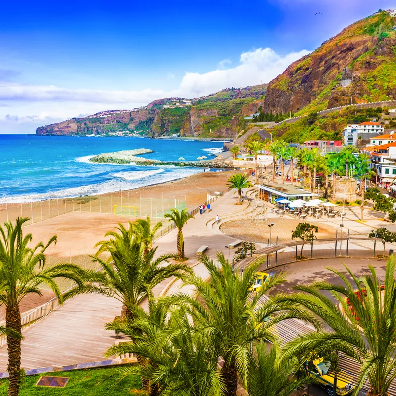 Strand mit Palmen und Bergen im Hintergrund an einem sonnigen Tag.