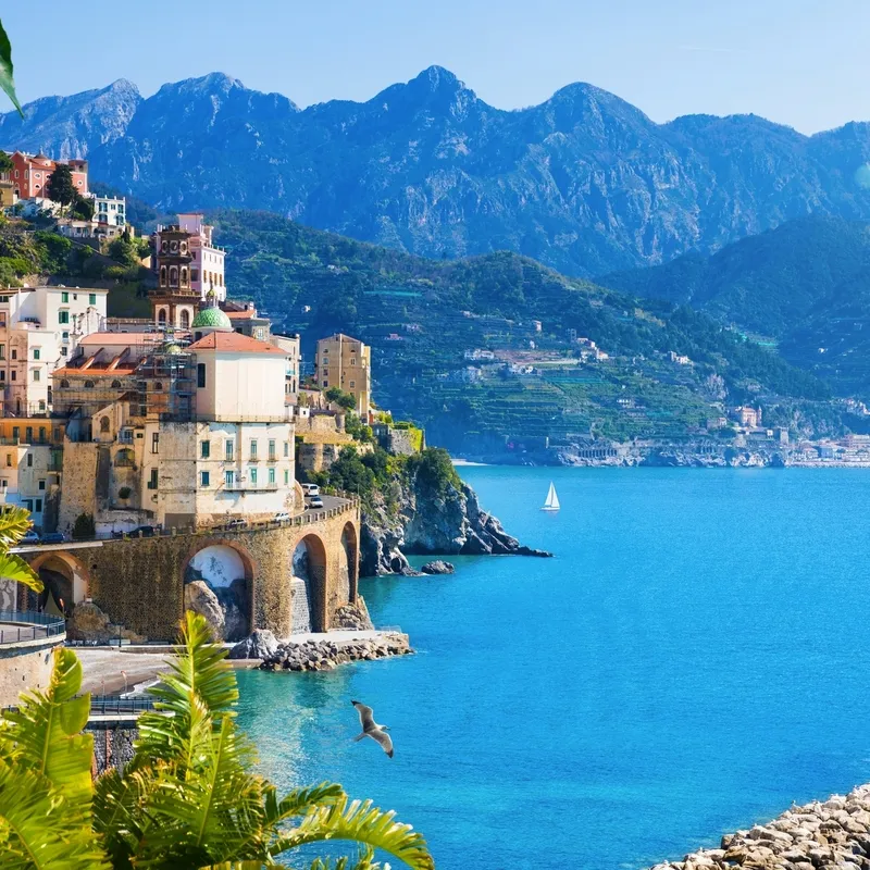 Küstenstadt mit bunten Gebäuden am Meer vor Bergkulisse.