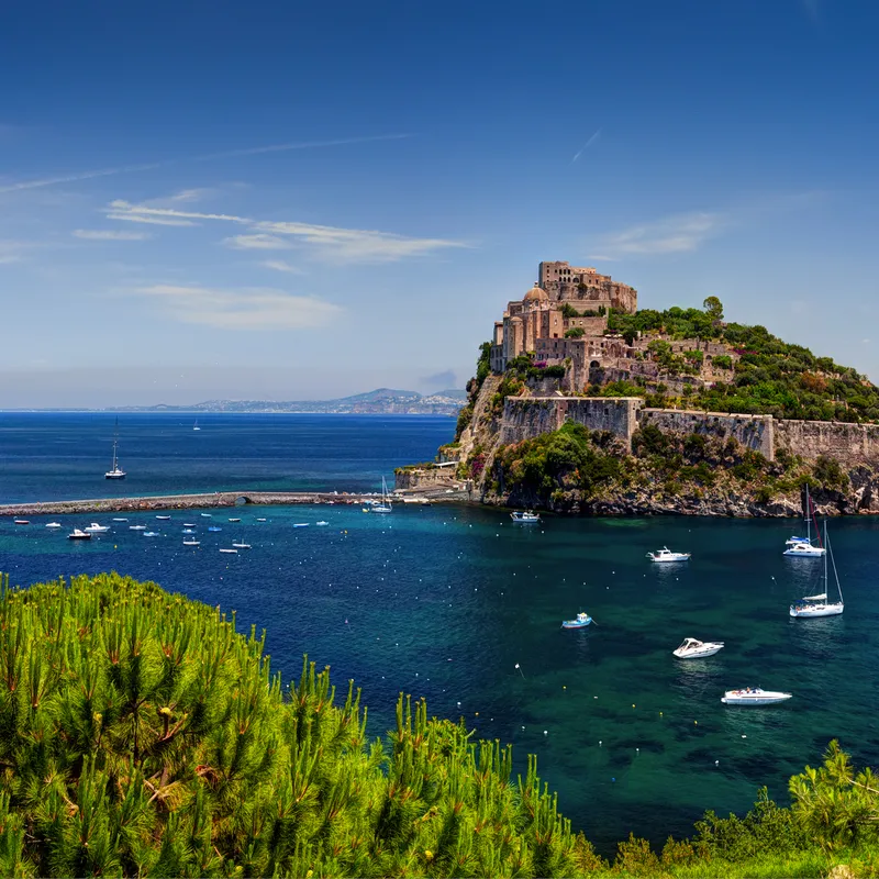Blick auf die Insel Ischia mit Burg Aragonese und Booten im blauen Meer.