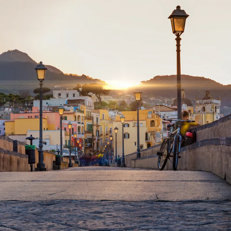Pflasterstraße mit Laternen, Fahrrad, im Hintergrund bunte Gebäude und Berge bei Sonnenaufgang