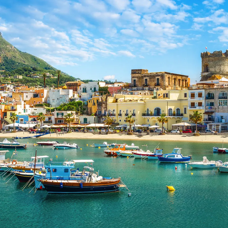 Boote im Hafen vor einer südeuropäischen Küstenstadt mit Bergen im Hintergrund.