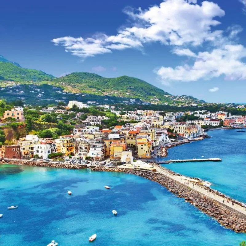 Blick auf eine mediterrane Küstenstadt mit bunten Häusern und klarem blauen Wasser.