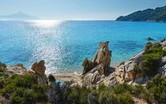 Küste mit Felsen und kristallklarem Wasser unter blauem Himmel.