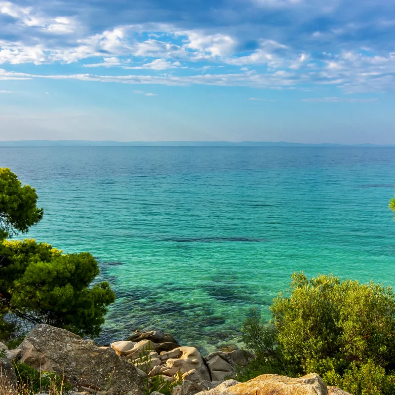 Blick auf das blaue Meer mit grünem Ufer und bewölktem Himmel.