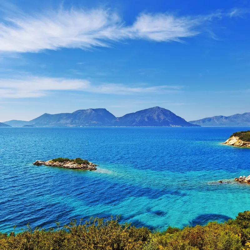 Blick auf blaues Meer mit Inseln und Bergen im Hintergrund bei klarem Himmel.