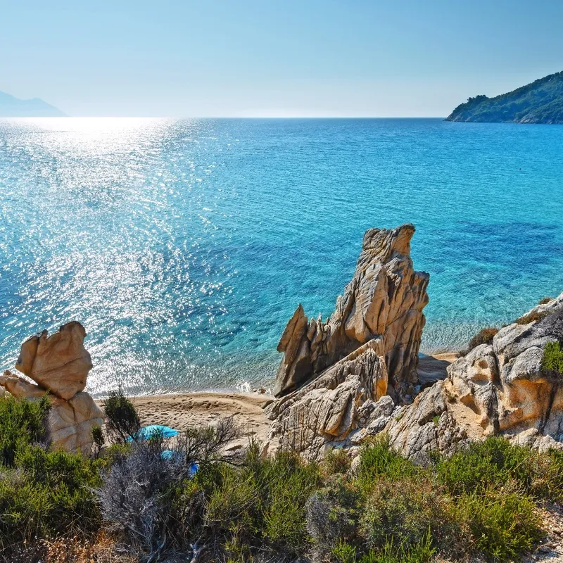 Küste mit Felsen und blauem Meer bei Sonnenschein.
