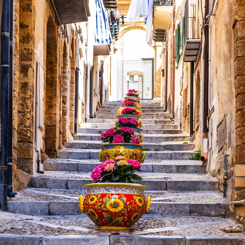 Steintreppe gesäumt von bunten Blumen in kunstvollen Töpfen in einer engen Gasse