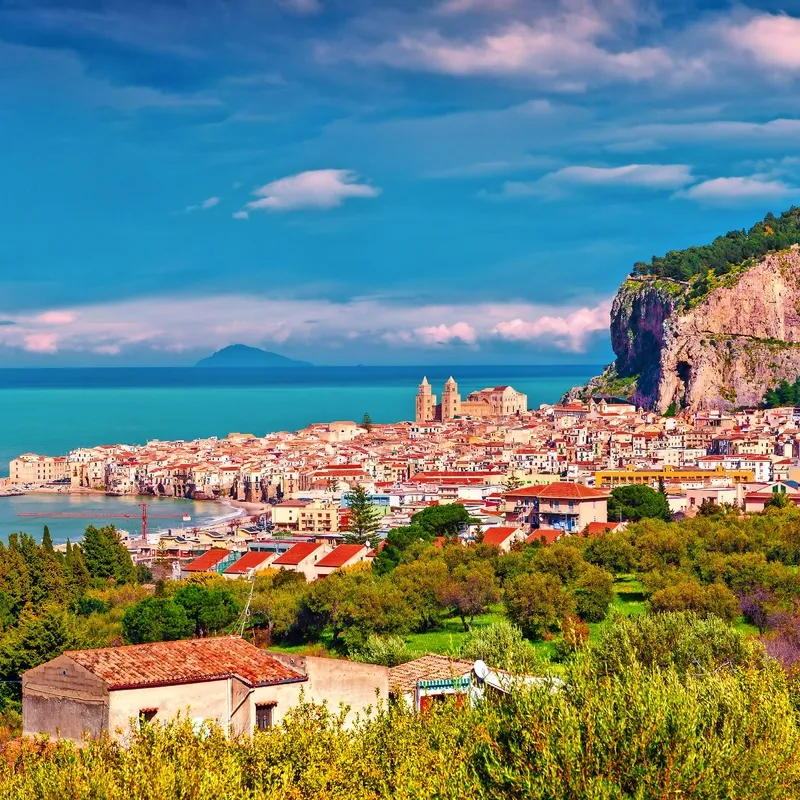 Küstenstadt mit Bergen, Meer und bewölktem Himmel im Hintergrund.