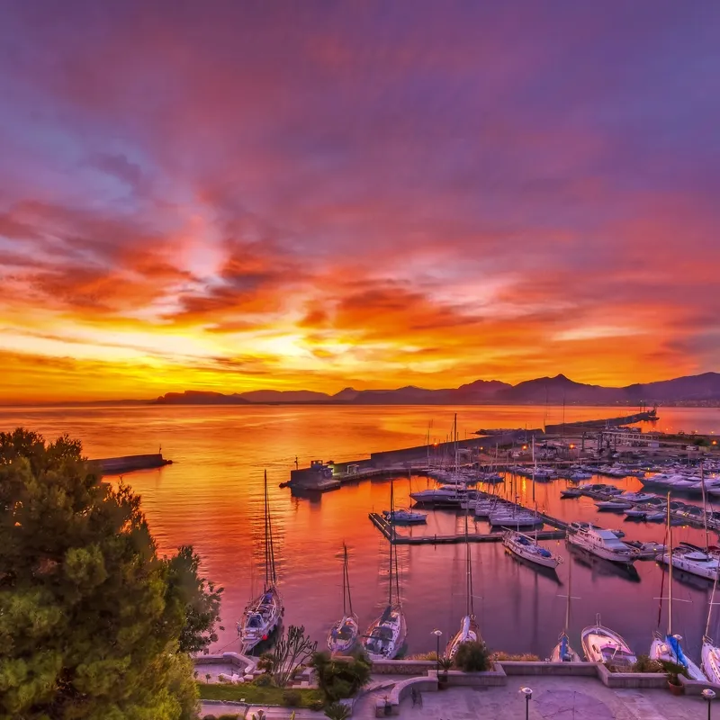 Sonnenuntergang über einem Hafen mit Segelbooten und buntem Himmel.