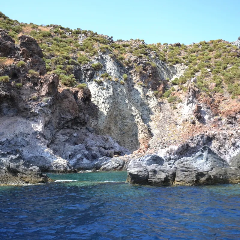 Steilküste mit grün bewachsenen Hügeln am Meer bei klarem Himmel.