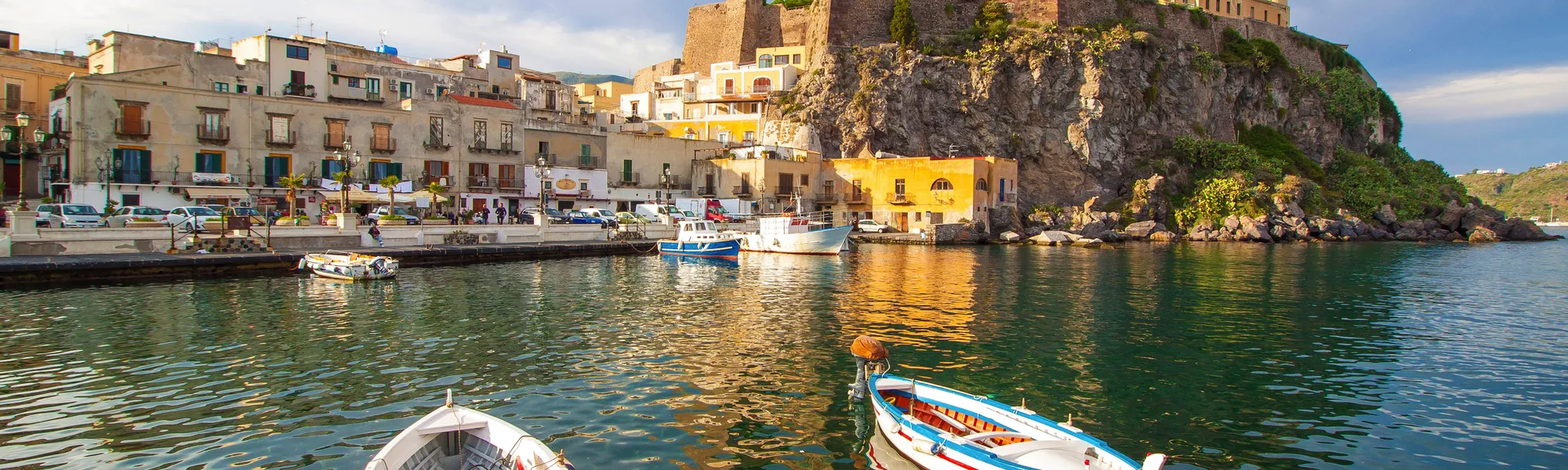 Boote im Hafen vor historischer Festung auf einem Hügel bei Sonnenschein