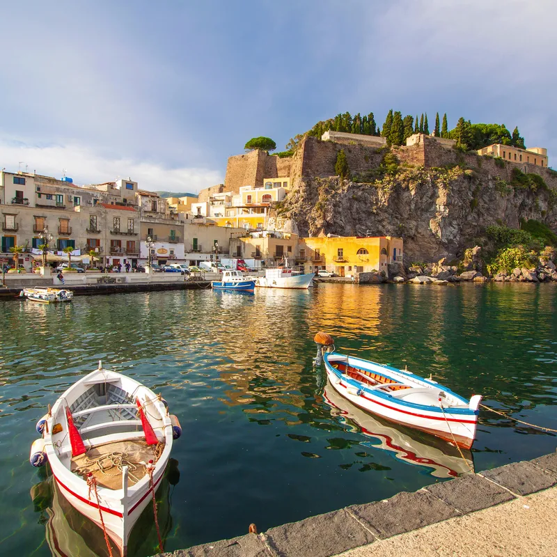 Boote im Hafen vor historischer Festung auf einem Hügel bei Sonnenschein