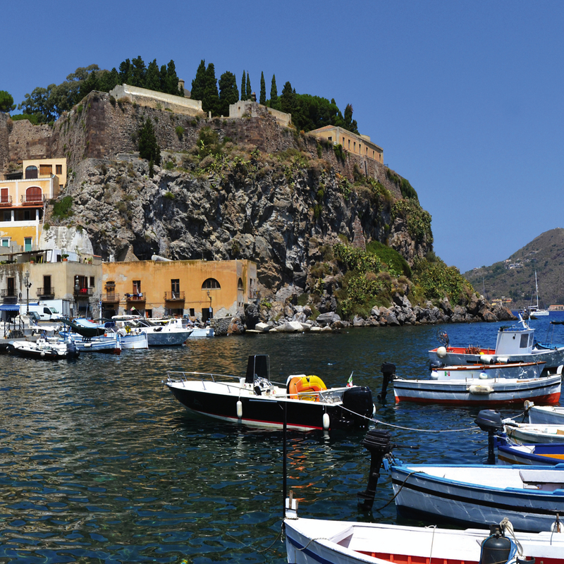 Hafen mit Booten vor einer Felsklippe auf den Liparischen Inseln, Italien.