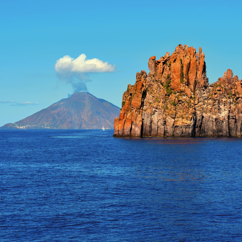 Küstenlandschaft mit Vulkan Stromboli und Felsen im Meer bei den Liparischen Inseln.