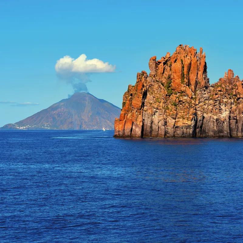 Küstenlandschaft mit Vulkan Stromboli und Felsen im Meer bei den Liparischen Inseln.