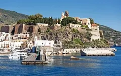 Küstenstadt mit Kirche auf einem Hügel, Boote im Hafen, sonnige Landschaft.