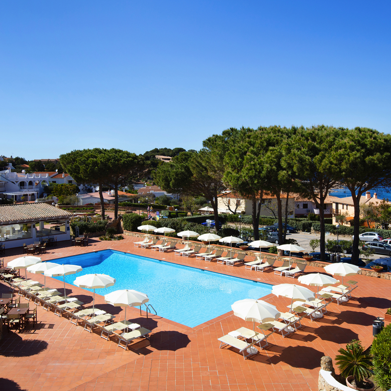 Poolbereich des Club Hotel Cormorano auf Sardinien mit Sonnenschirmen und Meerblick.
