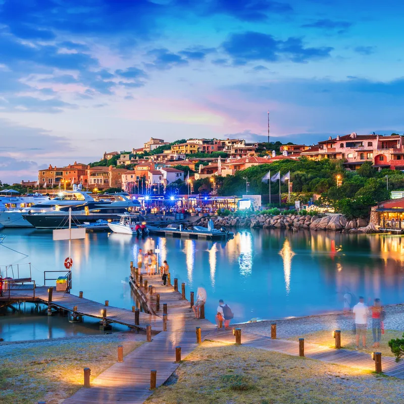 Hafen mit Yachten und Gebäuden bei Sonnenuntergang an einer Küste.