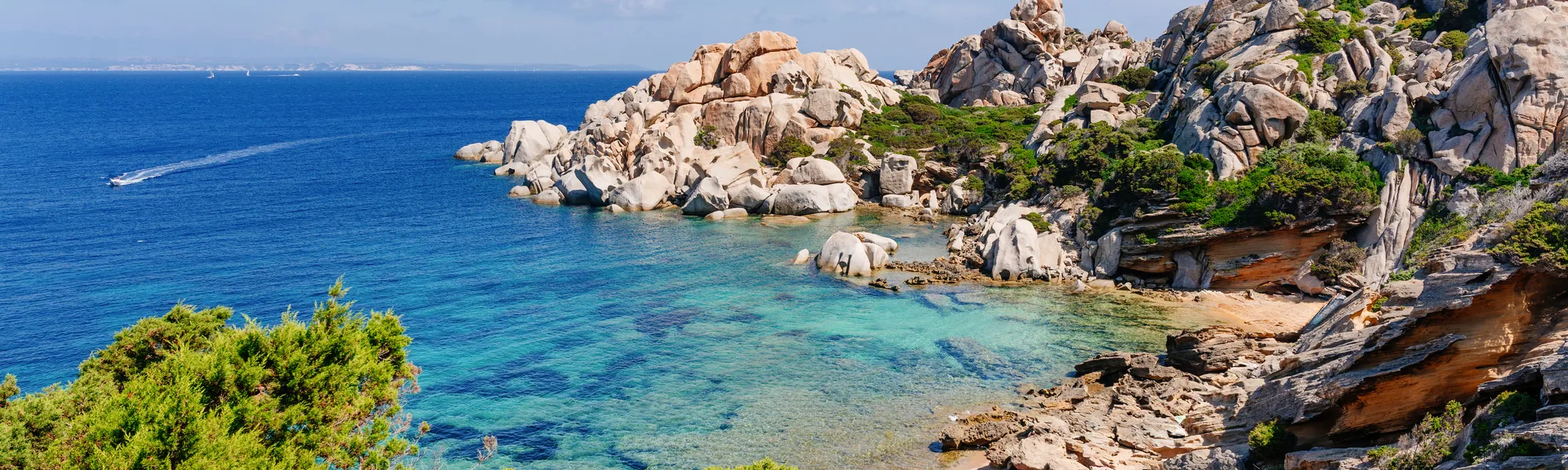 Felsige Küste mit klarem, blauem Meer unter blauem Himmel.