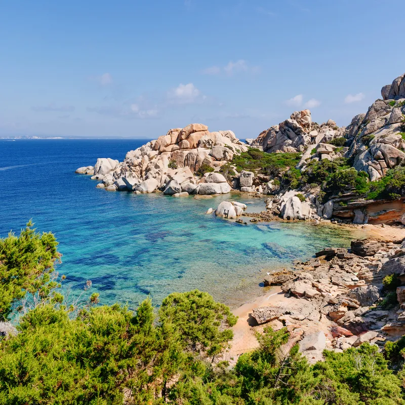 Felsige Küste mit klarem, blauem Meer unter blauem Himmel.