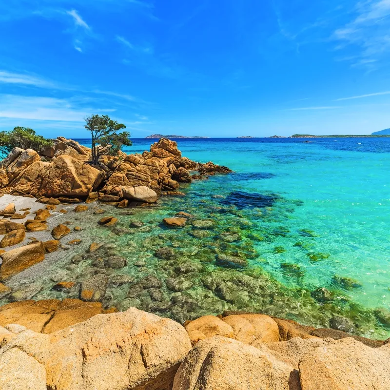 Küste mit türkisblauem Meer und Felsen unter blauem Himmel.