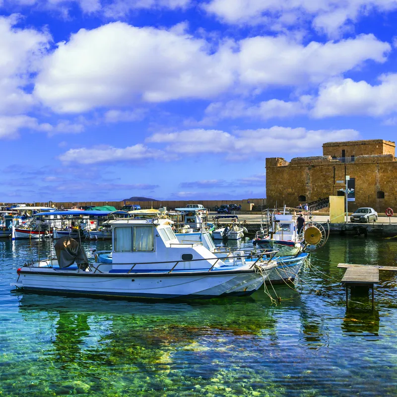 Historische Festung am Hafen mit Booten und klarem Wasser unter blauem Himmel.