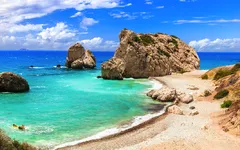 Küstenlandschaft mit Felsen und türkisblauem Meer unter blauem Himmel.