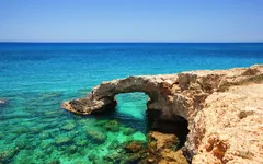 Steinbogen an der Küste mit klarem türkisfarbenem Meer und blauem Himmel im Hintergrund