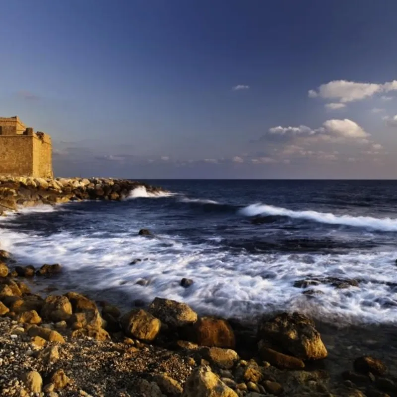 Steinige Küste Zyperns mit altem Gebäude am Meer unter blauem Himmel.