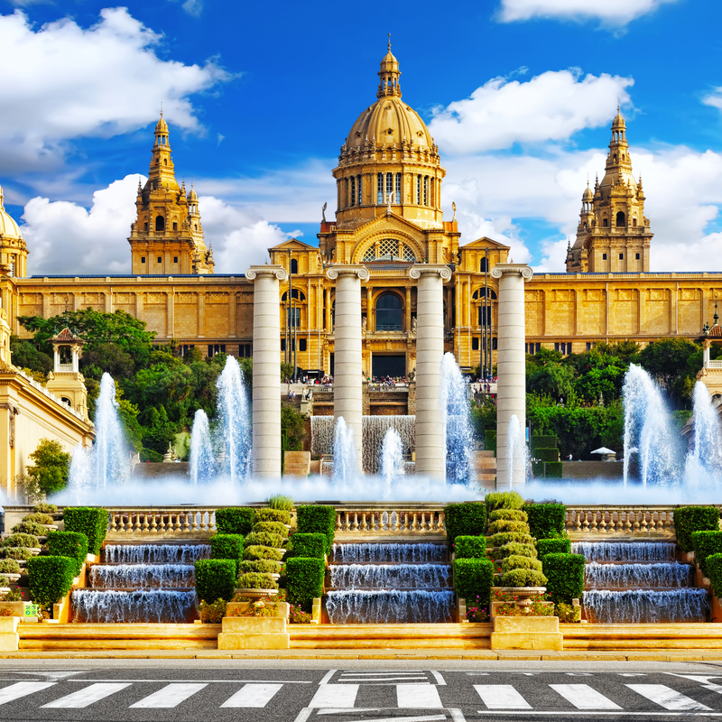 Historisches Gebäude mit Brunnen und Treppen vor blauem Himmel.