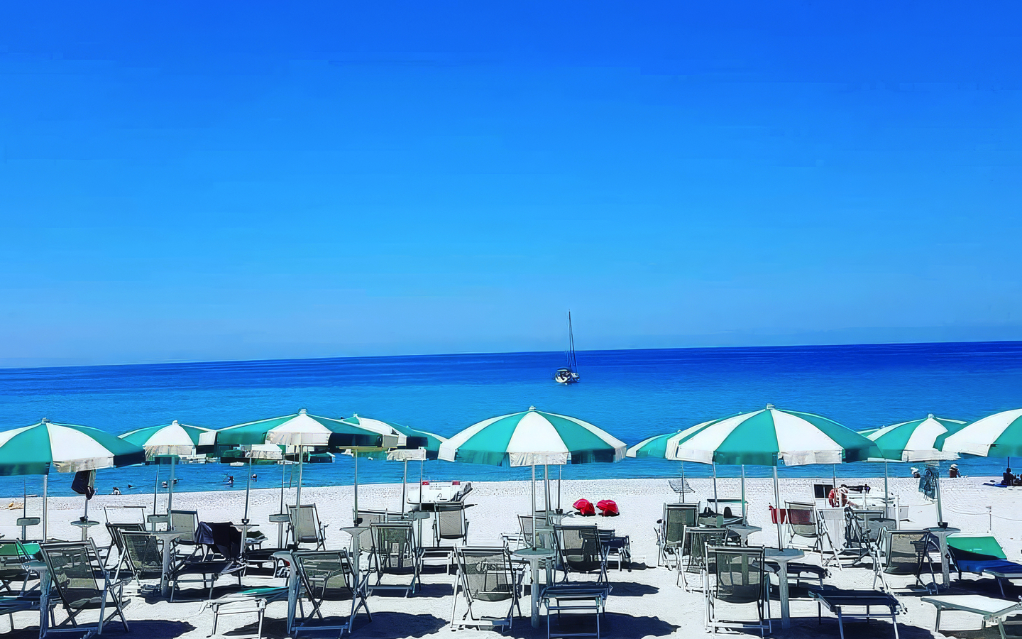 Strand mit Sonnenliegen und -schirmen am blauen Meer in Kalabrien, Italien.