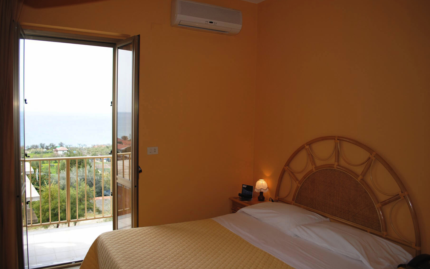 Hotelzimmer mit Doppelbett, Balkon mit Meerblick, gelbe Wände und Klimaanlage.