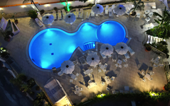 Außenpool bei Nacht im Hotel La Praia, Italien, umgeben von Liegestühlen und Sonnenschirmen.