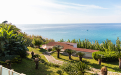 Blick auf einen Garten mit Palmen und das Meer im Hintergrund, Kalabrien, Italien.