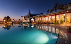 Hotel mit beleuchtetem Pool bei Abenddämmerung und Palmen in Kalabrien, Italien.