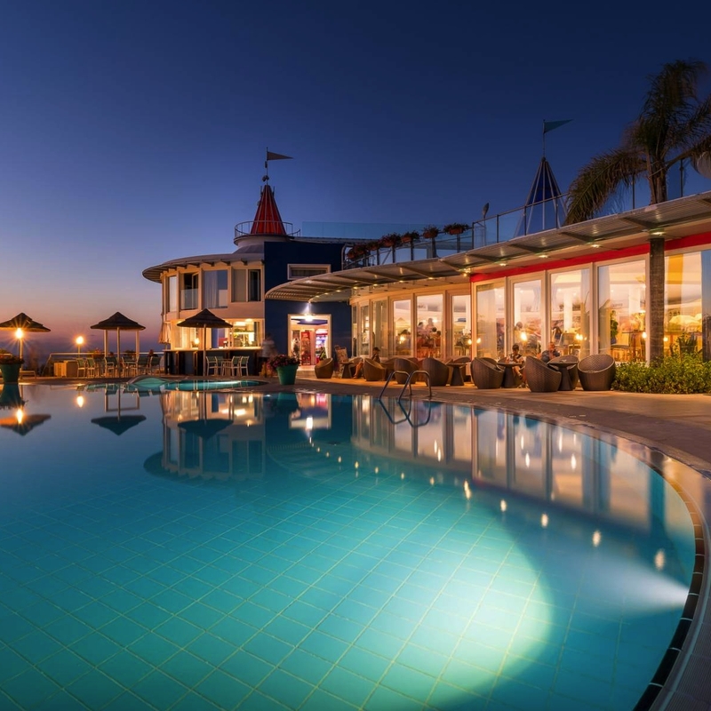 Hotel mit beleuchtetem Pool bei Abenddämmerung und Palmen in Kalabrien, Italien.