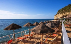 Sonnenschirme und Liegestühle am Sandstrand mit Meerblick bei klarem Himmel.