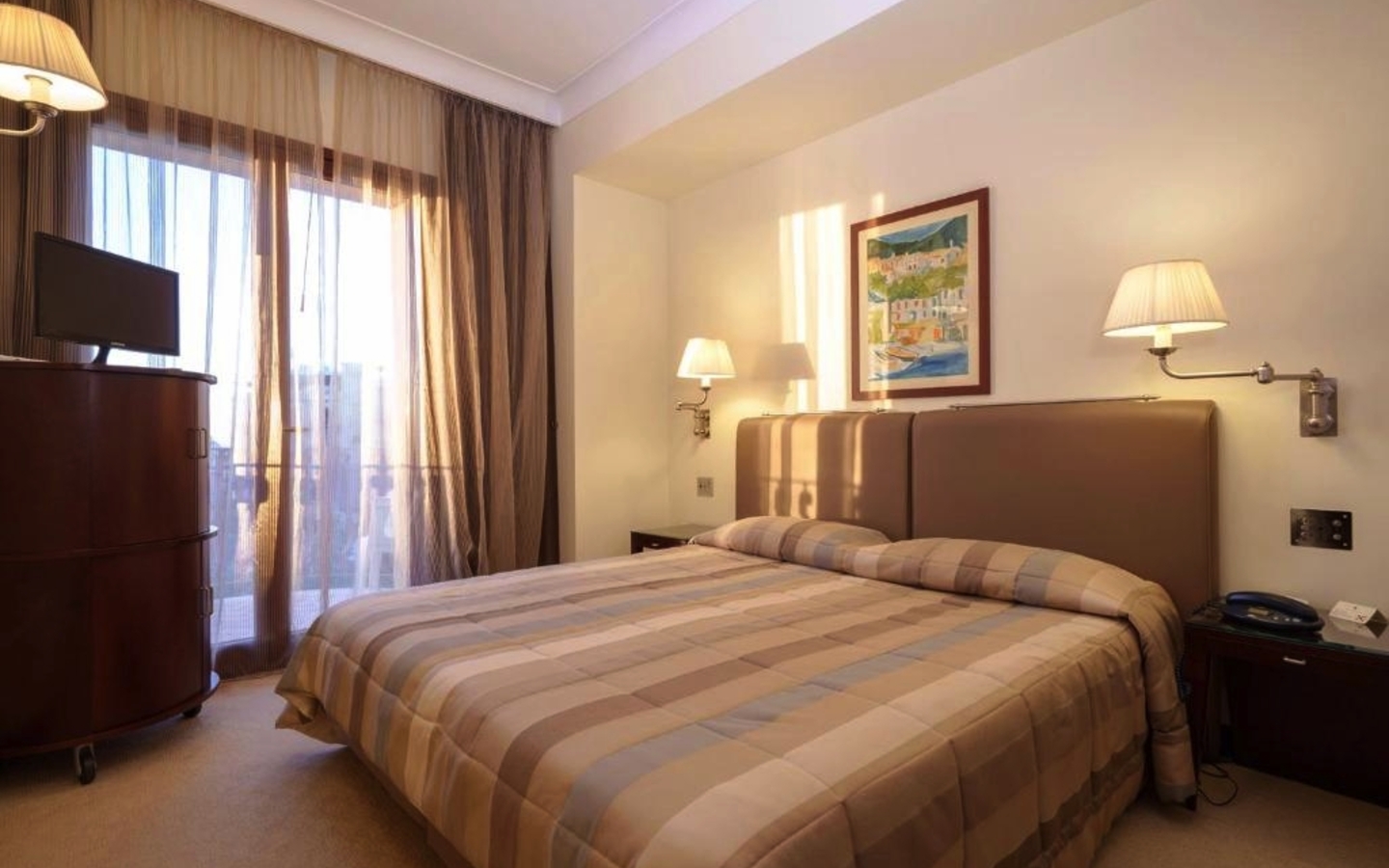 Doppelzimmer im Hotel mit großem Bett, Nachttischlampen und Blick auf den Balkon.