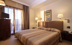 Doppelzimmer im Hotel mit großem Bett, Nachttischlampen und Blick auf den Balkon.