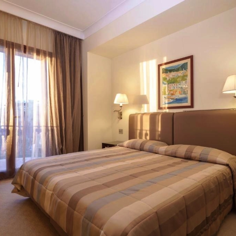 Doppelzimmer im Hotel mit großem Bett, Nachttischlampen und Blick auf den Balkon.