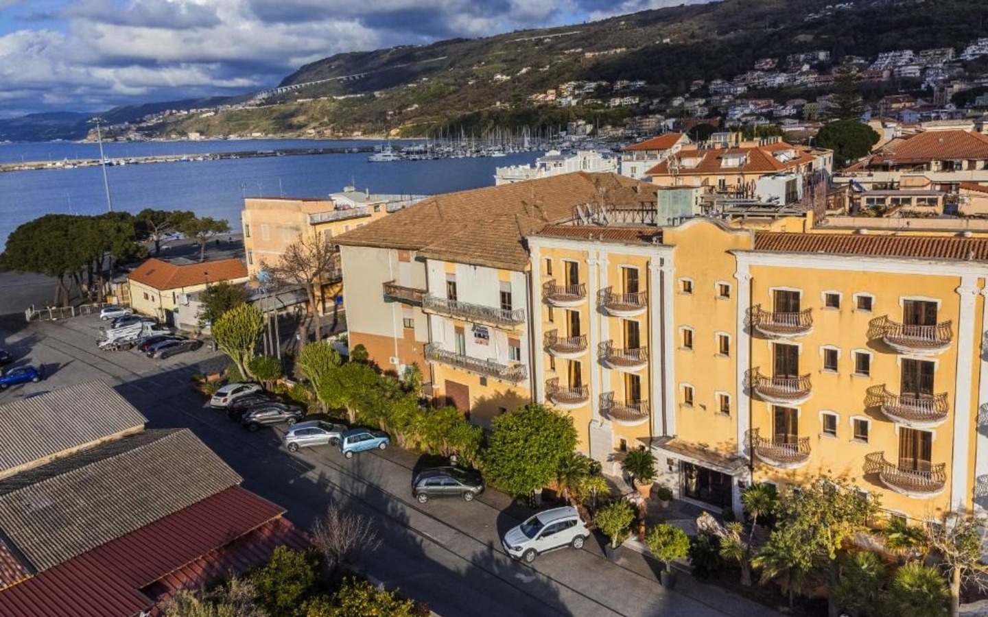 Hotelgebäude nahe der Küste mit Blick auf das Meer und Hügel im Hintergrund.