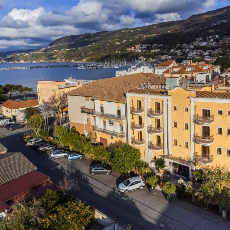 Hotelgebäude nahe der Küste mit Blick auf das Meer und Hügel im Hintergrund.