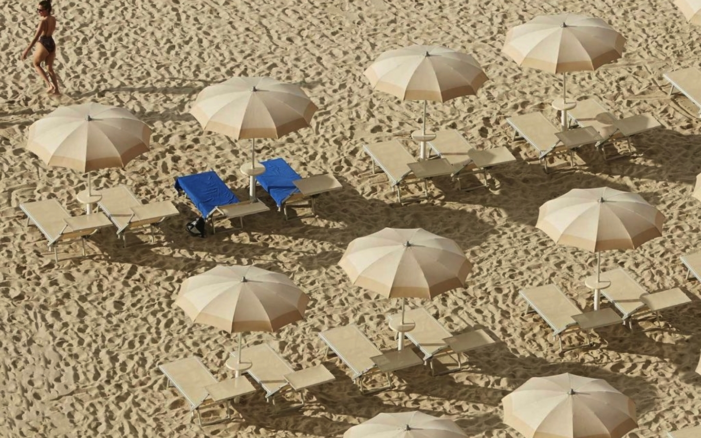 Strand mit Sonnenschirmen und Liegen, Person spaziert am Sand entlang.