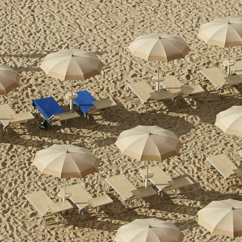 Strand mit Sonnenschirmen und Liegen, Person spaziert am Sand entlang.